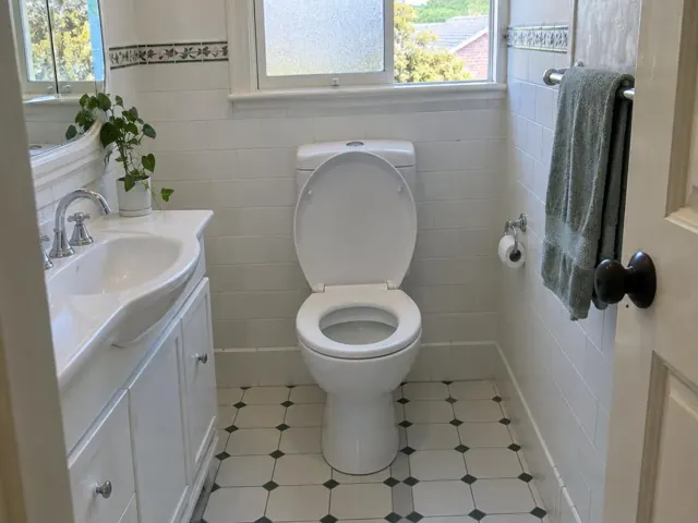 Clean white toilet in a tiled family bathroom with vanity and window in Balgowlah