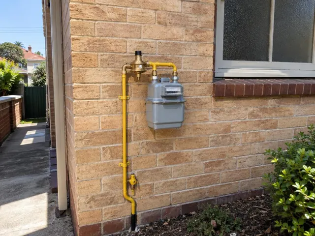 External gas meter and yellow pipework on a brick brick wall beside a window in Fairlight