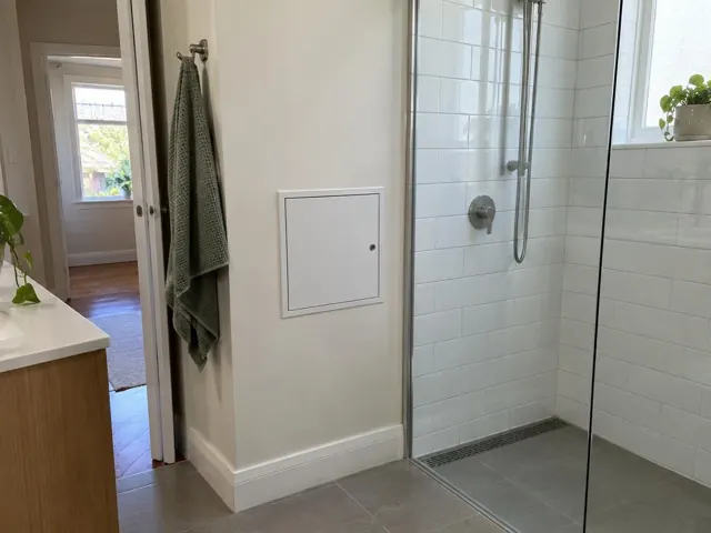 Bathroom wall with a small access panel beside a glass shower in a tiled room in Balgowlah